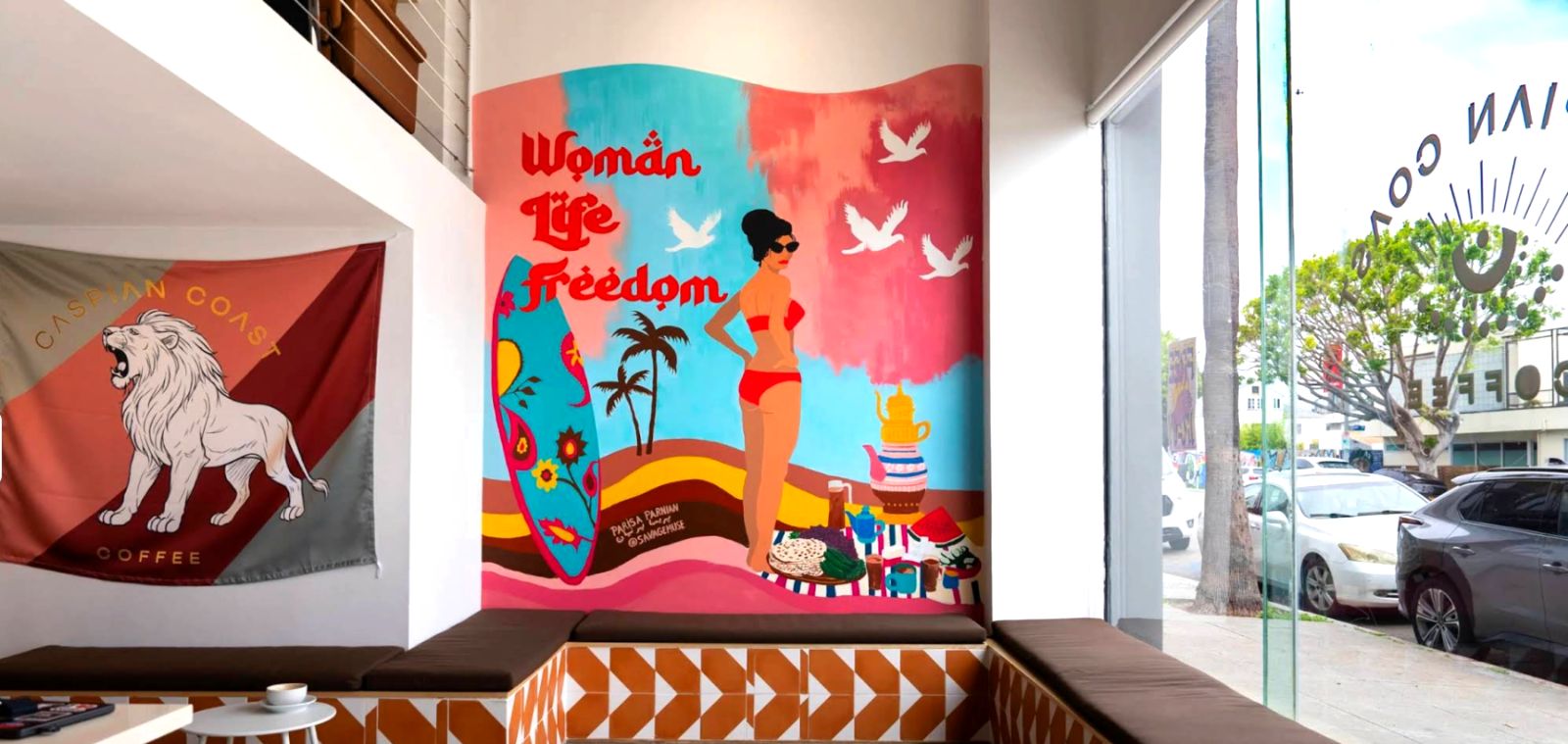Inside Caspian Coast Coffee, Venice — the Woman Life Freedom mural by Parisa Parnian, the Caspian Coast lion flag, and tiled bench seating by the window